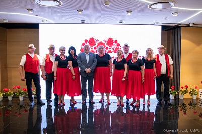 Kilka kobiet i mężczyzn w dojrzałym wieku pozują do zdjęcia w strojach ludowych, pośrodku między nimi stoi Marszałek Województwa Lubelskiego.