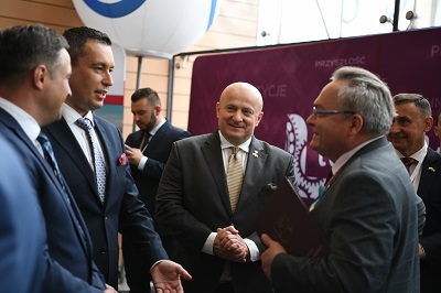 Czterech mężczyzn stojących i rozmawiających ze sobą w tle przewijające się inne osoby