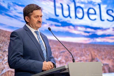 Mężczyzna stojący bokiem w sali konferencyjnej i udzielający wypowiedzi do stojącego przed nim mikrofonu. Członek Zarządu Województwa Lubelskiego Zdzisław Szwed