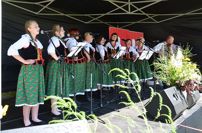 Młode kobiety ubrane w stroje ludowe stoją na scenie i śpiewają.