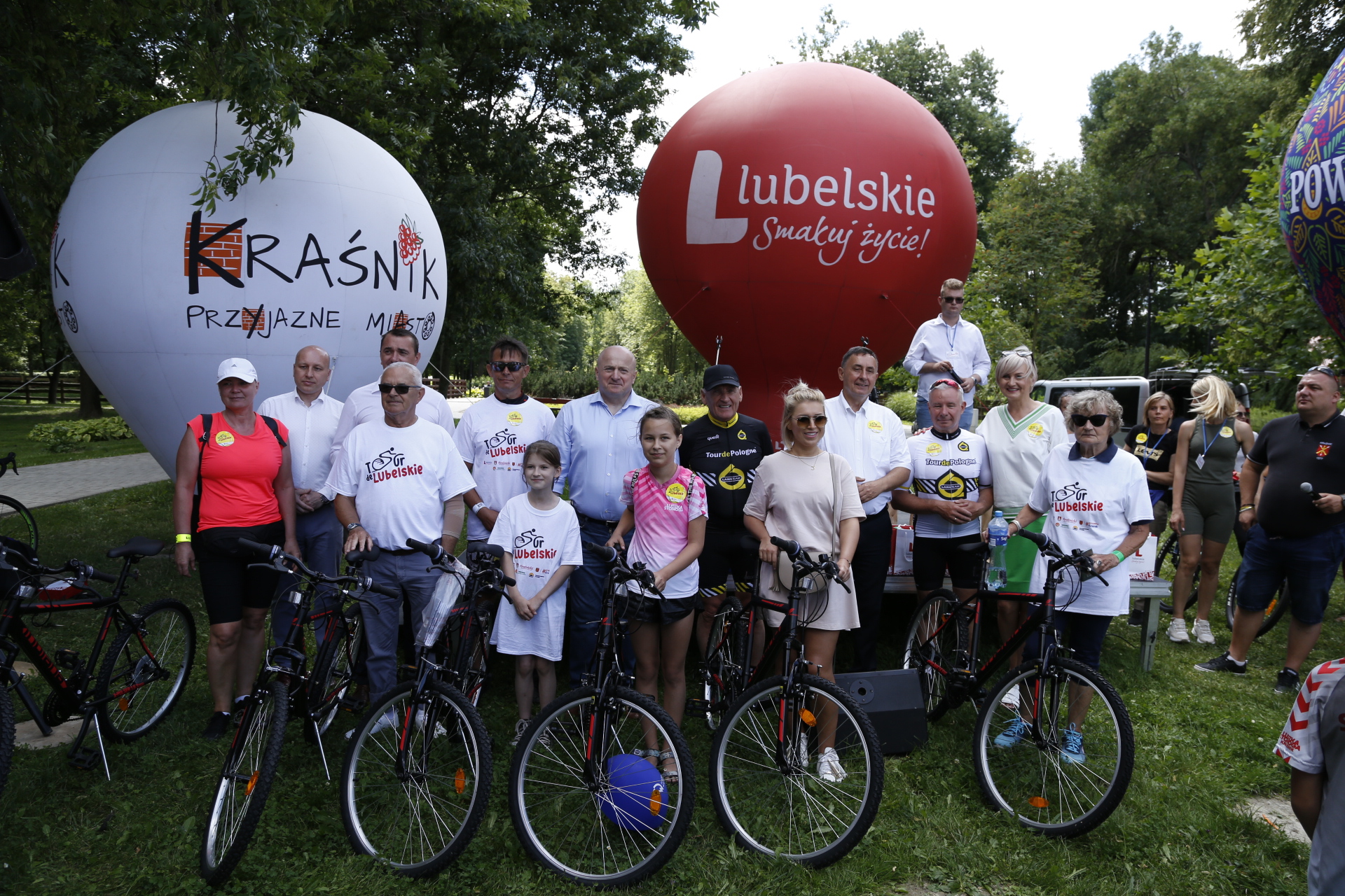 Grupa osób w róznym wieku, w trakcie festynu, pozują do zdjęcia z rowerami. Za nimi w tle balony z napisem lubelskie i Kraśnik