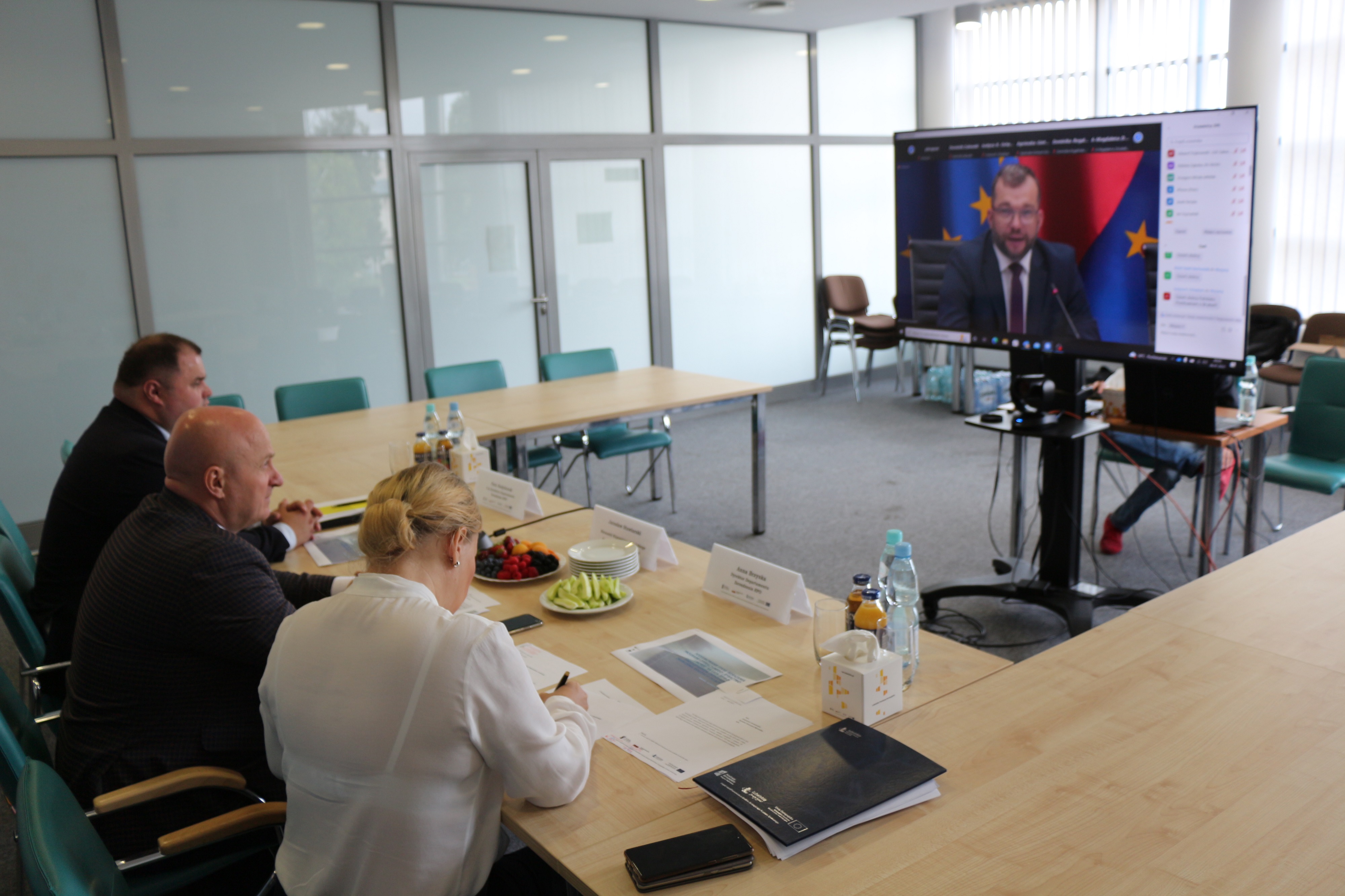 Widok na salę konferencyjną i konferencję zdalną z udziałem trzech mezczyzn i jednej kobiety