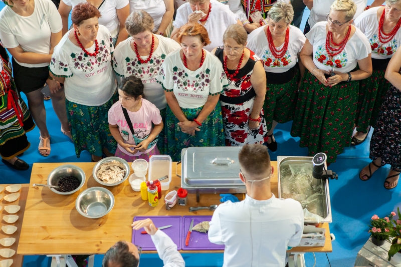 Widok z góry na stoisko z jedzeniem i sotjące przy nim kobiety w strojach ludowych.
