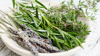 W białej misce leża gałązki różnych ziół. Miska stoi na drewnianym blacie