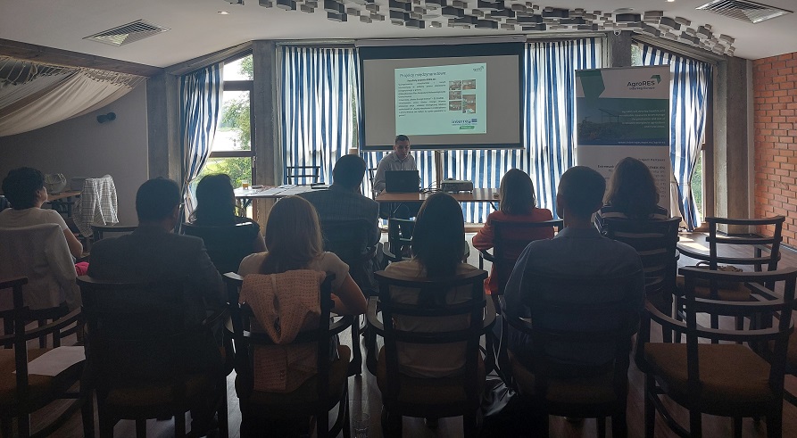 Widok na salę konferencyjną i uczestników spotkania oraz prowadzącego wykład i wyświetlany na ekranie omawiany temat