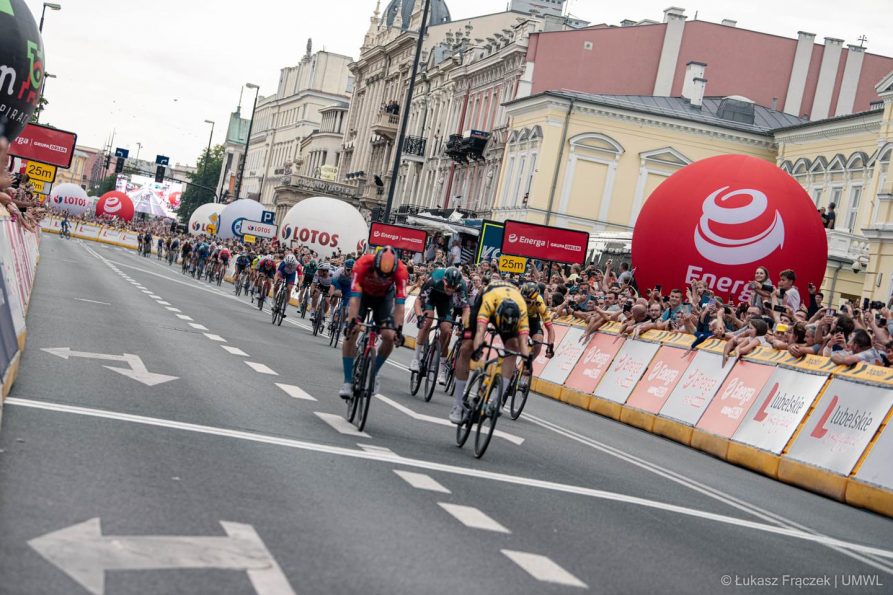 Duża grupa kolarzy przed linią mety na tle dopingujących kibiców