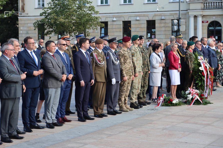 Uczestnicy spotkania stoją wszerz Placu Litewskiego. Przed nimi ułożone wieńce.