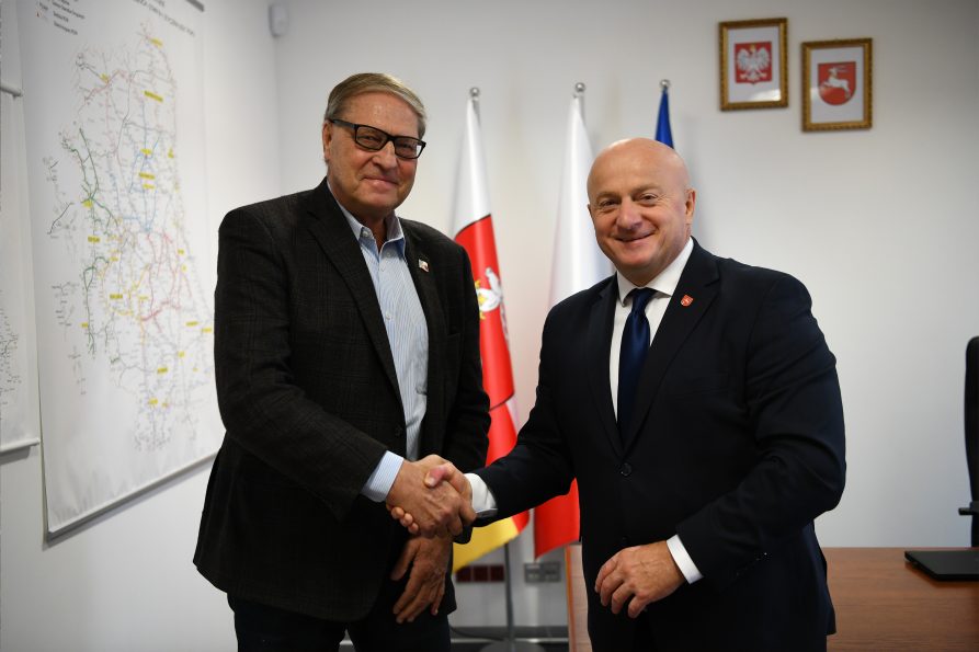 Dwóch mężczyzn w garniturze uściska sobie dłonie na tle flag