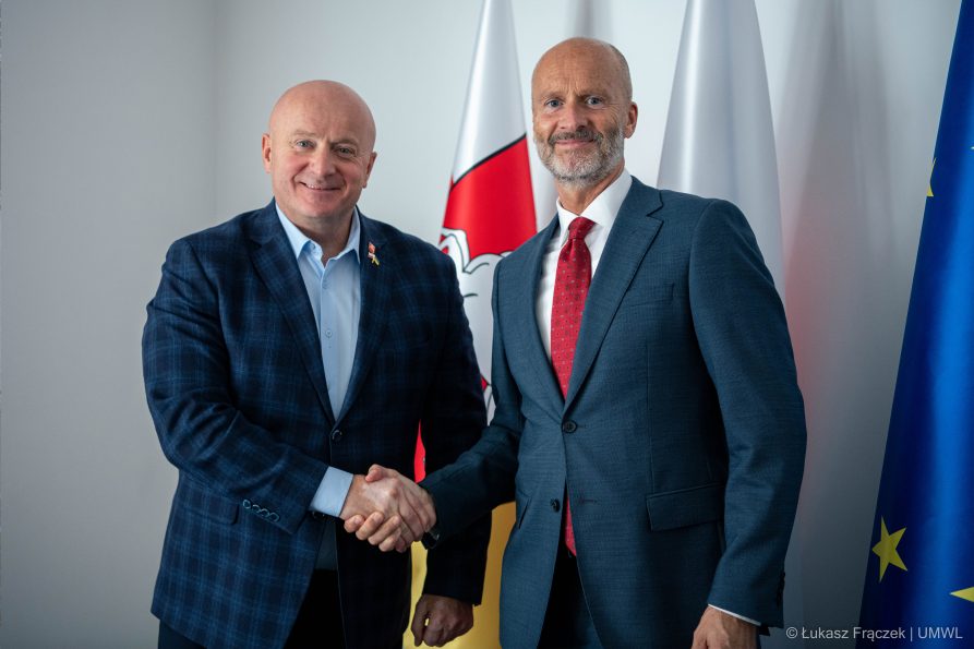 Dwóch mężczyzn w garniturze uściska sobie dłonie na tle flag