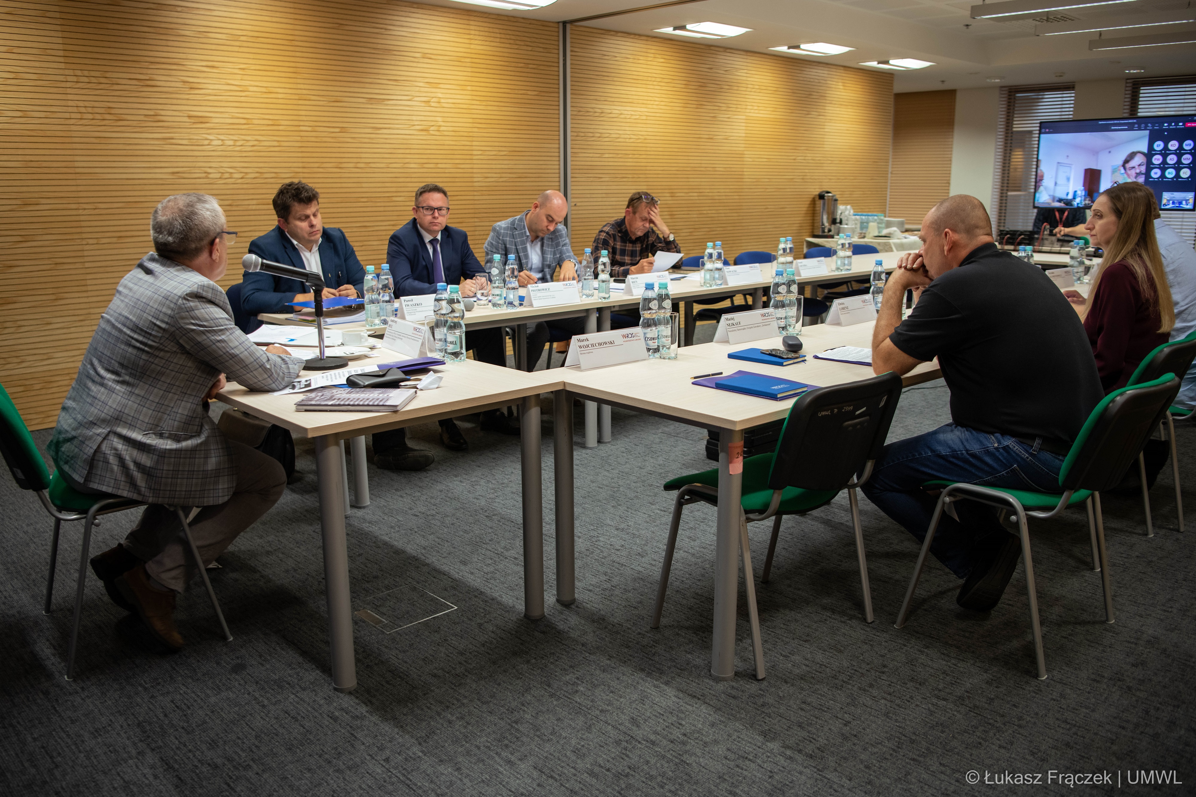 Widok na uczestników posiedzenia w sali konferencyjnej. Siedzą przy stołach i przeglądają notatki.