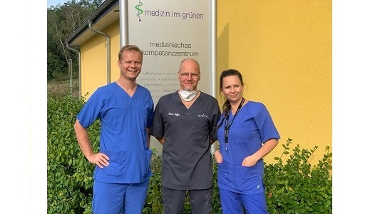 Trójka lekarz dwóch mężczyzn i kobieta w kitlach stoją na zewnątrz przed przychodnią