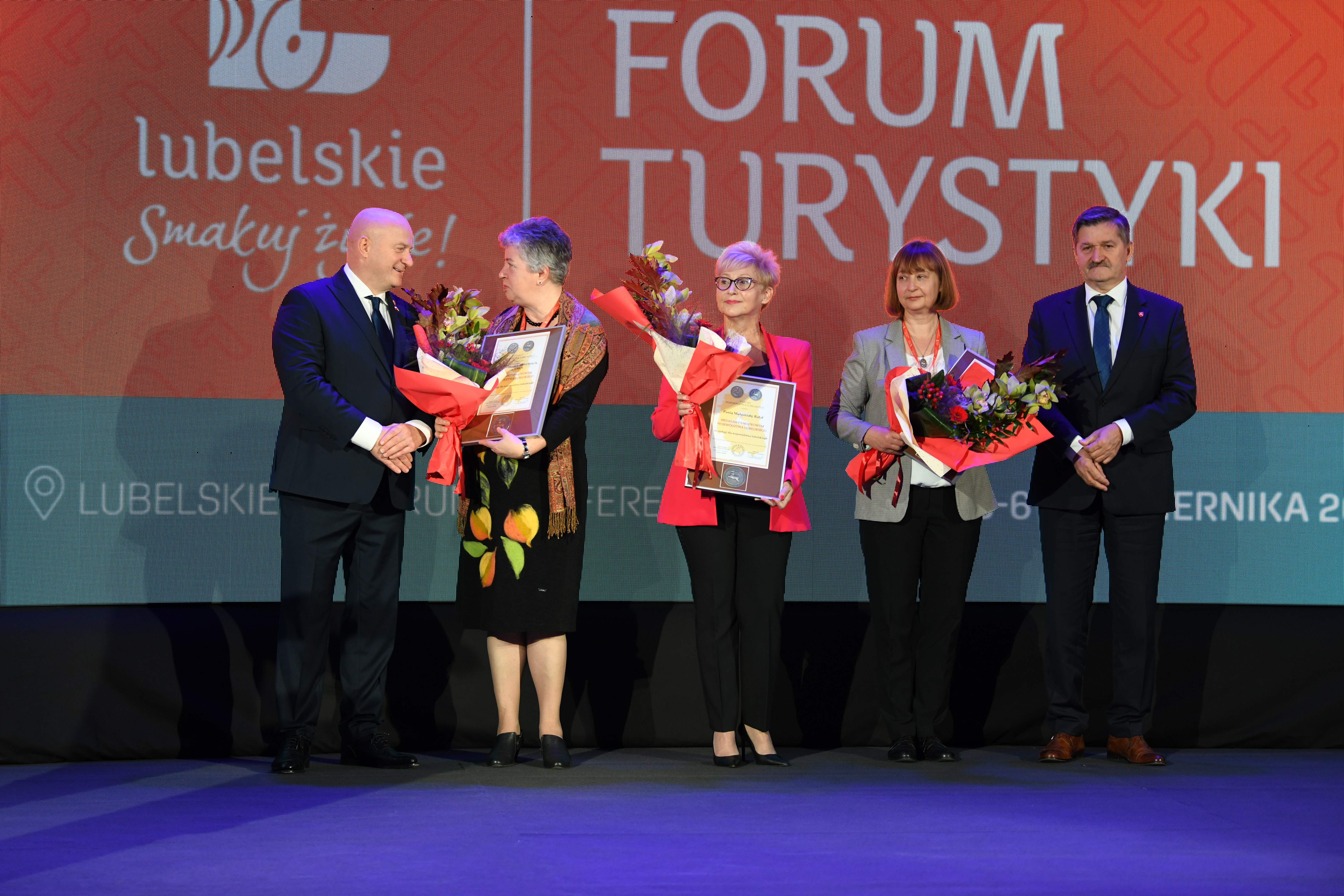 Widok na scenę w sali konferencyjnej przedstawiciele samorządu wraz z nagrodzonymi medalami pamiatkowymi