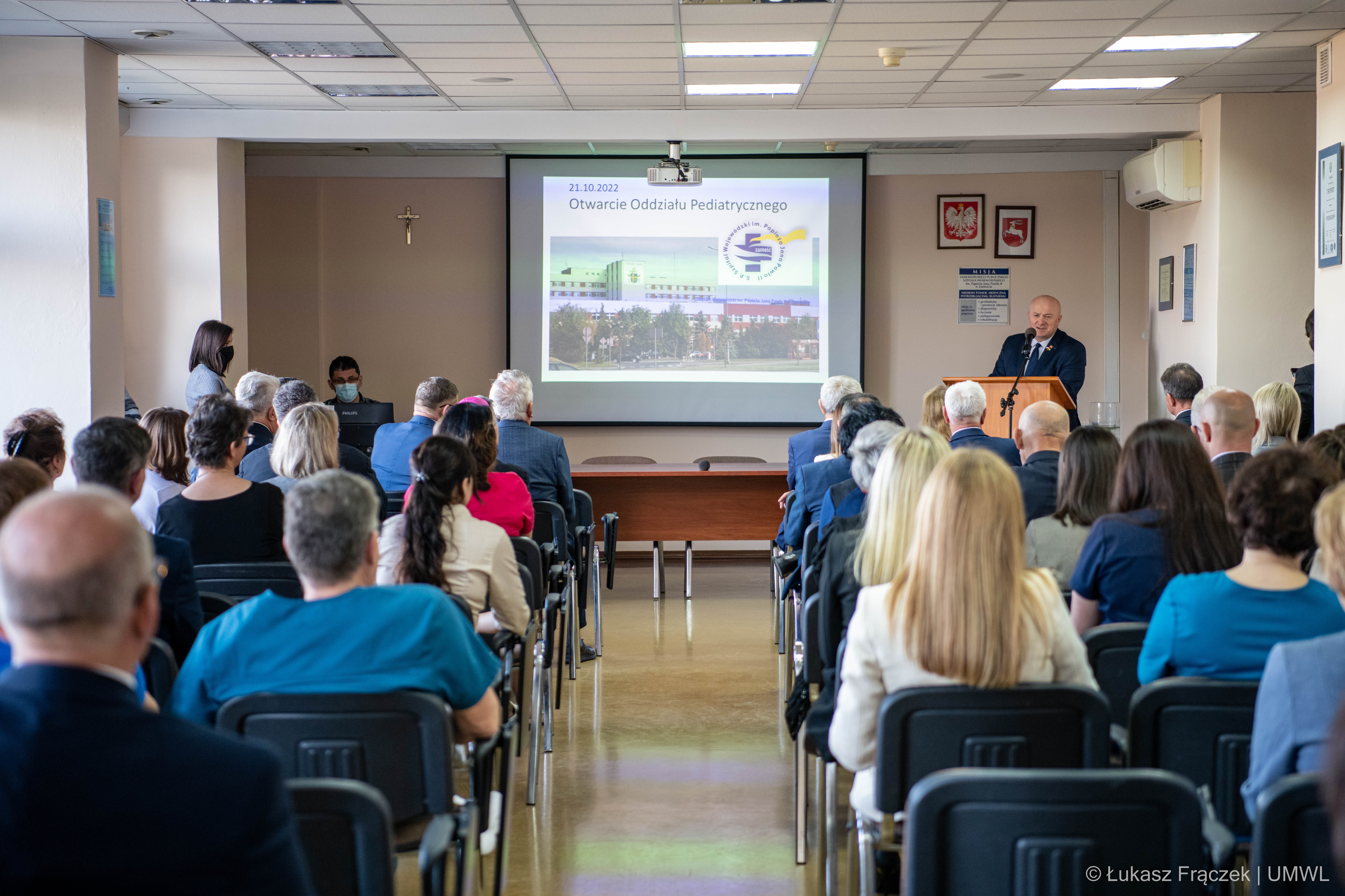 Sala szpitalna wypełniona gośćmi z okazji otwarcia oddziału i marszałek WL wyglaszający przemowienie