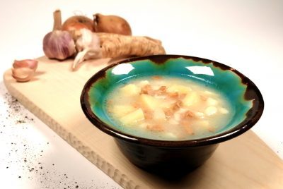 Na drewnianej desce w talerzu prezentuje się "trawnicka zaciera" - rodzaj tradycyjnej polewki z Trawnik. Zupa na bazie ziemniaków, rwanych klusek oraz okrasy. W tle zielonego talerza z zupą widoczne przyprawy.