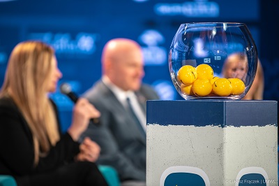 Widok na szklany wazon w którym widoczne są żółte piłeczki zawierające nazwy zespołów