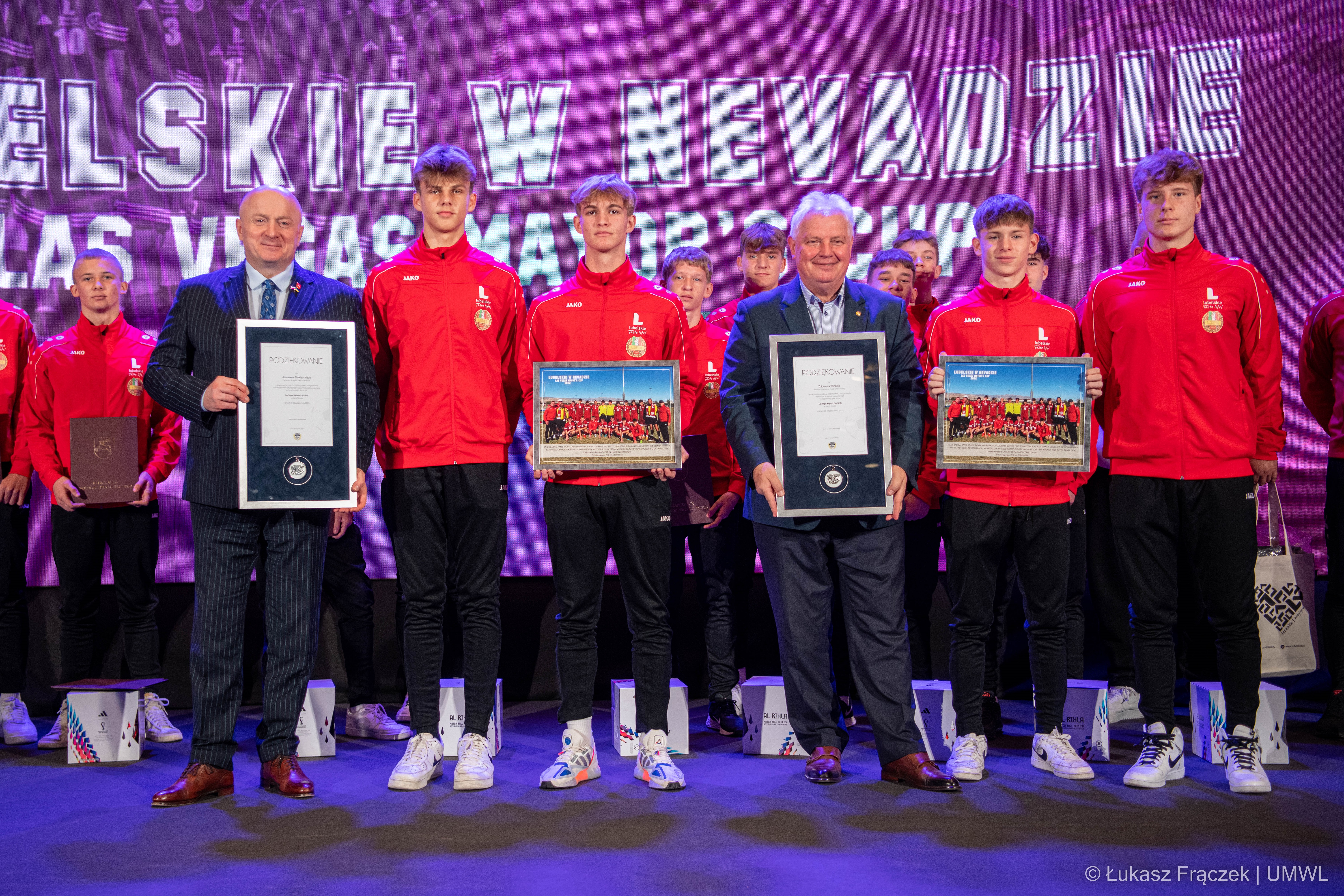 Marszałek WL prezentuje podziękowania które otrzymał ,w tle drużyna piłkarska