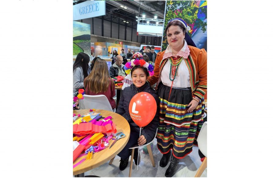 Kobieta w stroju ludowym pozuje do zdjęcia z małą dziewczynką trzymającą balon