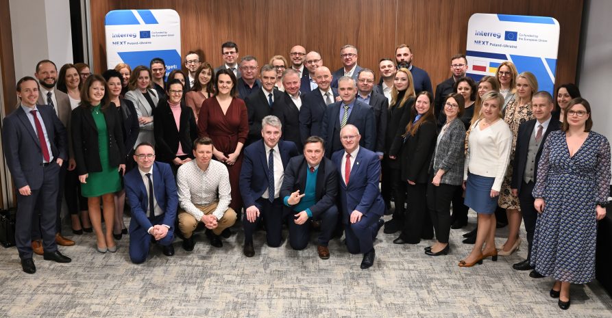 Członkowie komitetu monitorującego (około 50 osób) na tle roll upu nowego programu Interreg NEXT Polska-Ukraina 2021-2027ls