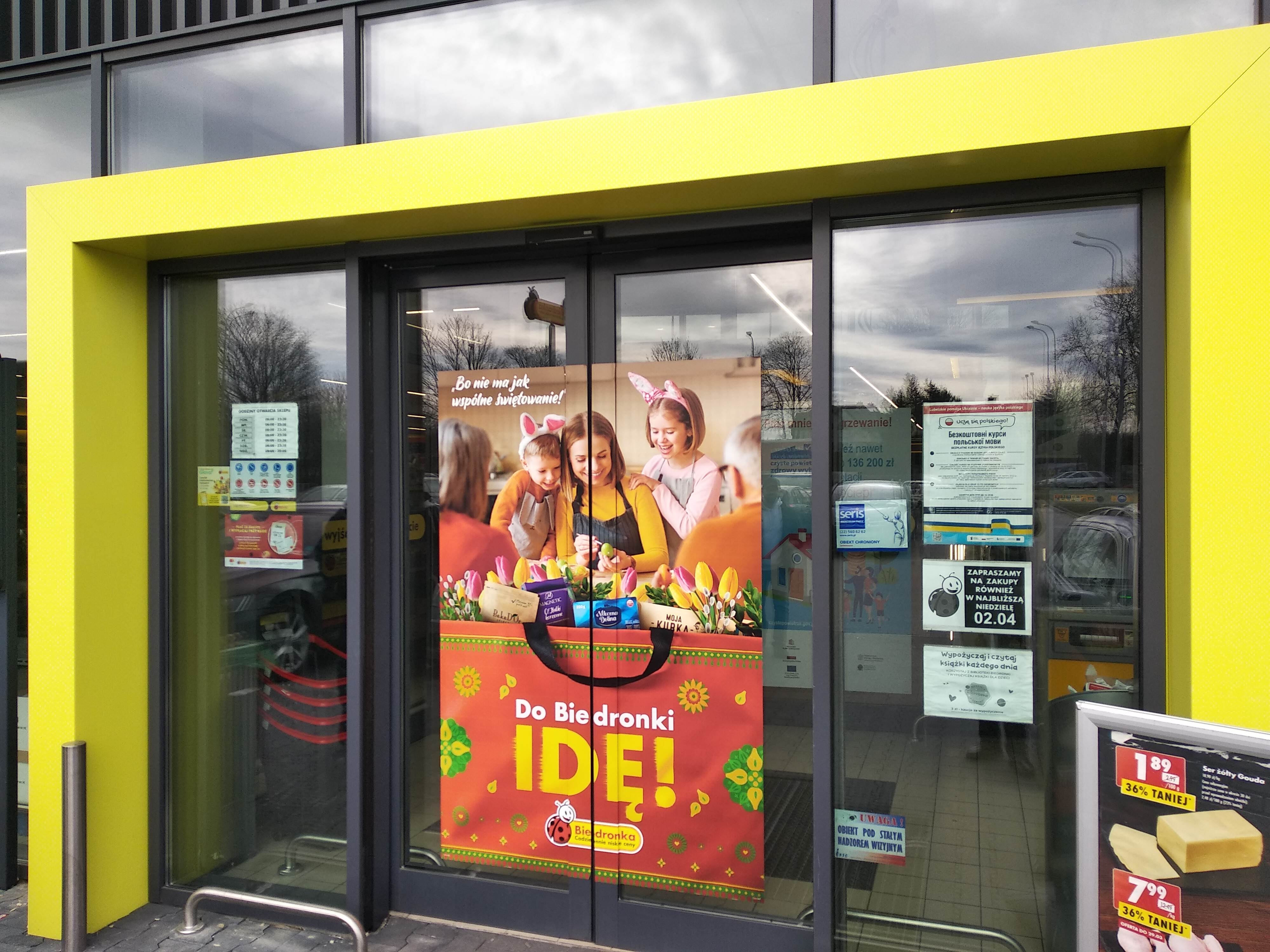 Wejście do sklepu biedronka z plakatem projektu nauki języka polskiego dla Ukrainy
