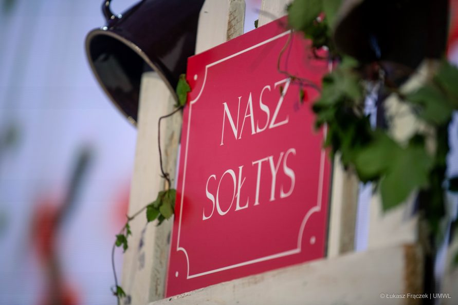 Symboliczna tabliczka z napisem Nasz Sołtys powieszona na drewnianym płocie