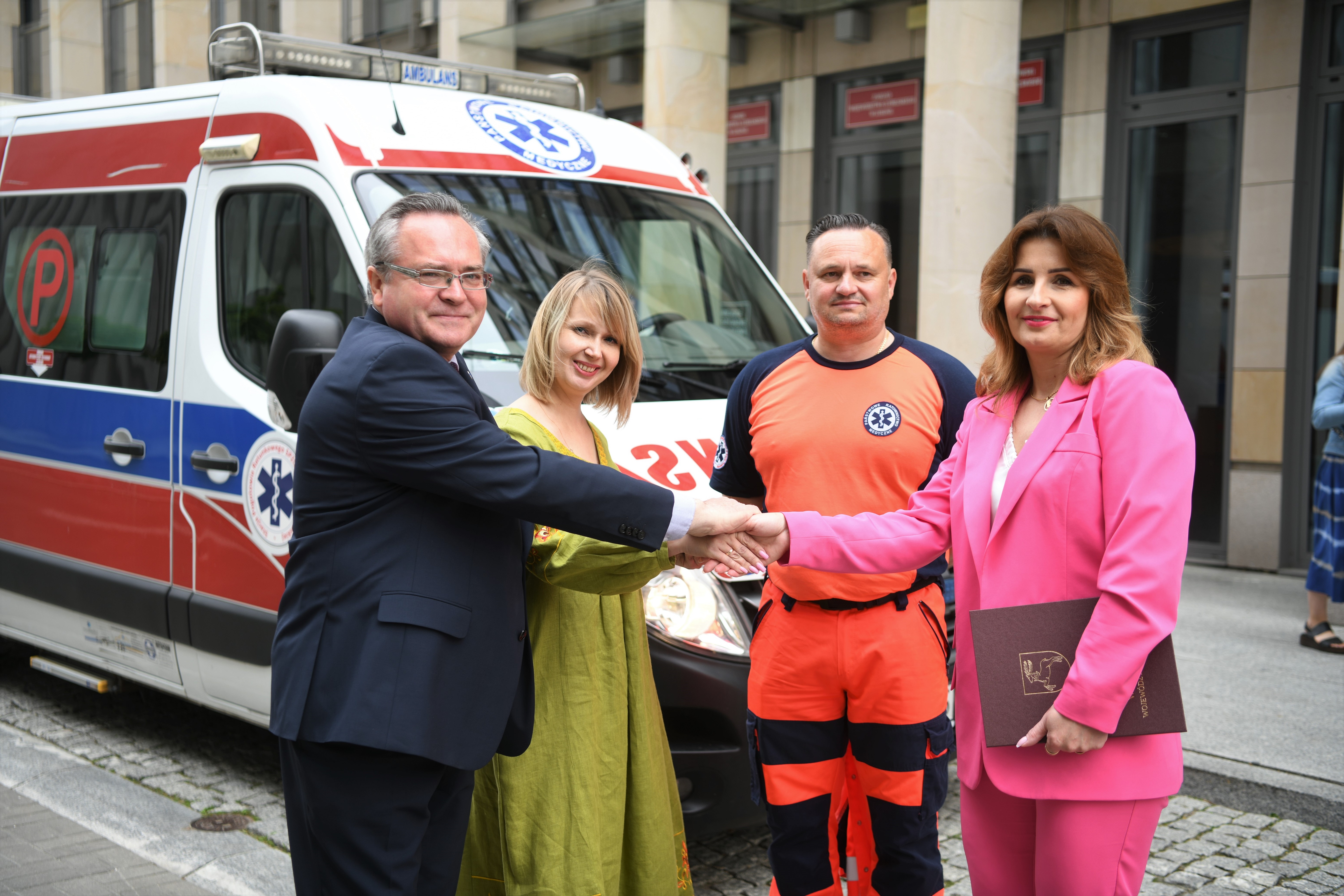 Uczestnicy przekazania ambulansu wspólnie pozują do zdjęcia przed siedzibą urzędu