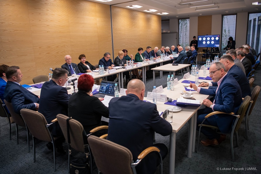 Członkowie rady siedzą przy stole ustawionym w podkowę