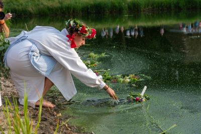 kobieta w wianku i białej sukience puszczająca wianek na wodę