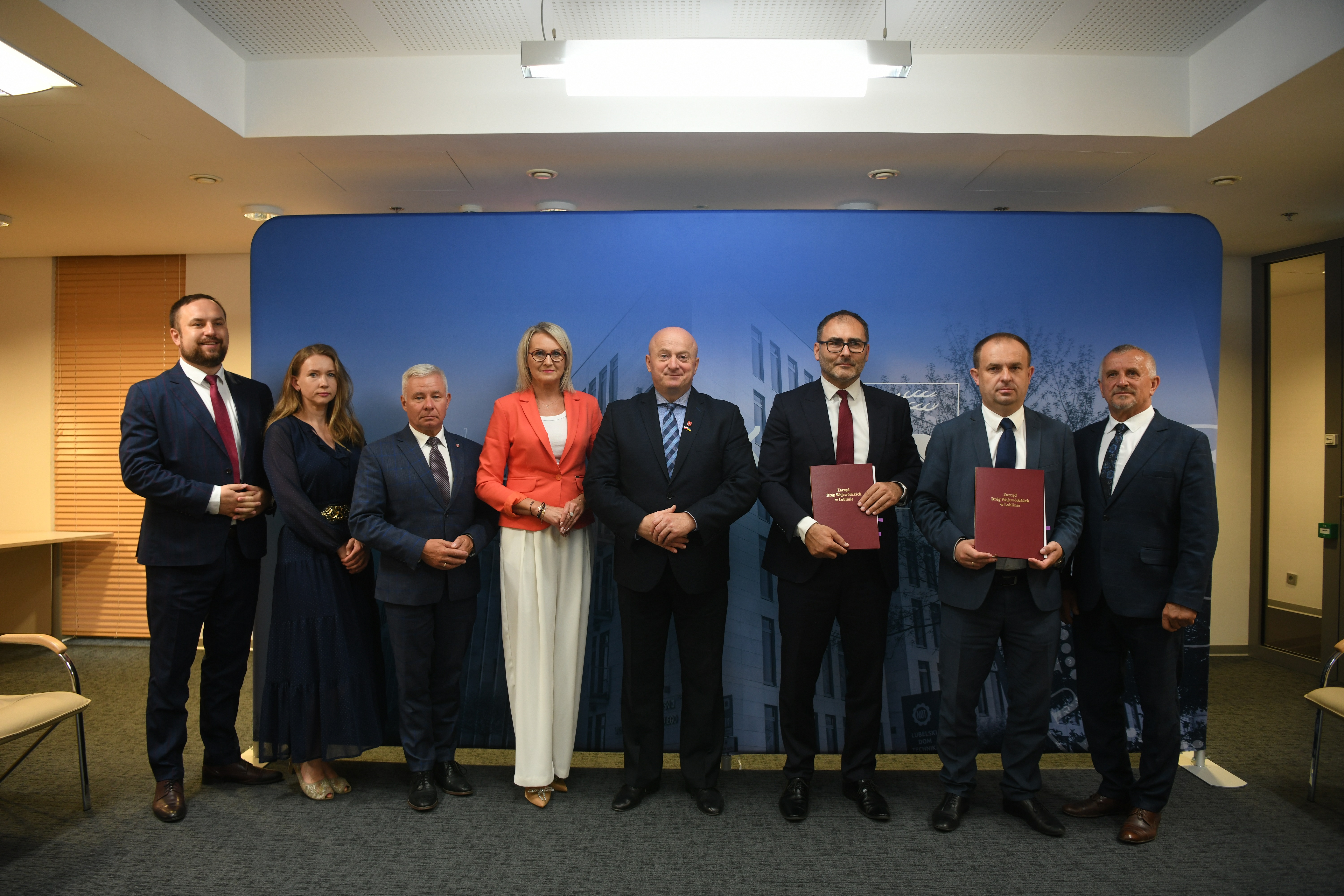 Około 10 osób pozujacych do zdjęcia na ściance Urzędu Marszałkowskiego. Uczestnicy spotkania dot. opracowania koncepcji budowy zachodniej obwodnicy Kraśnika