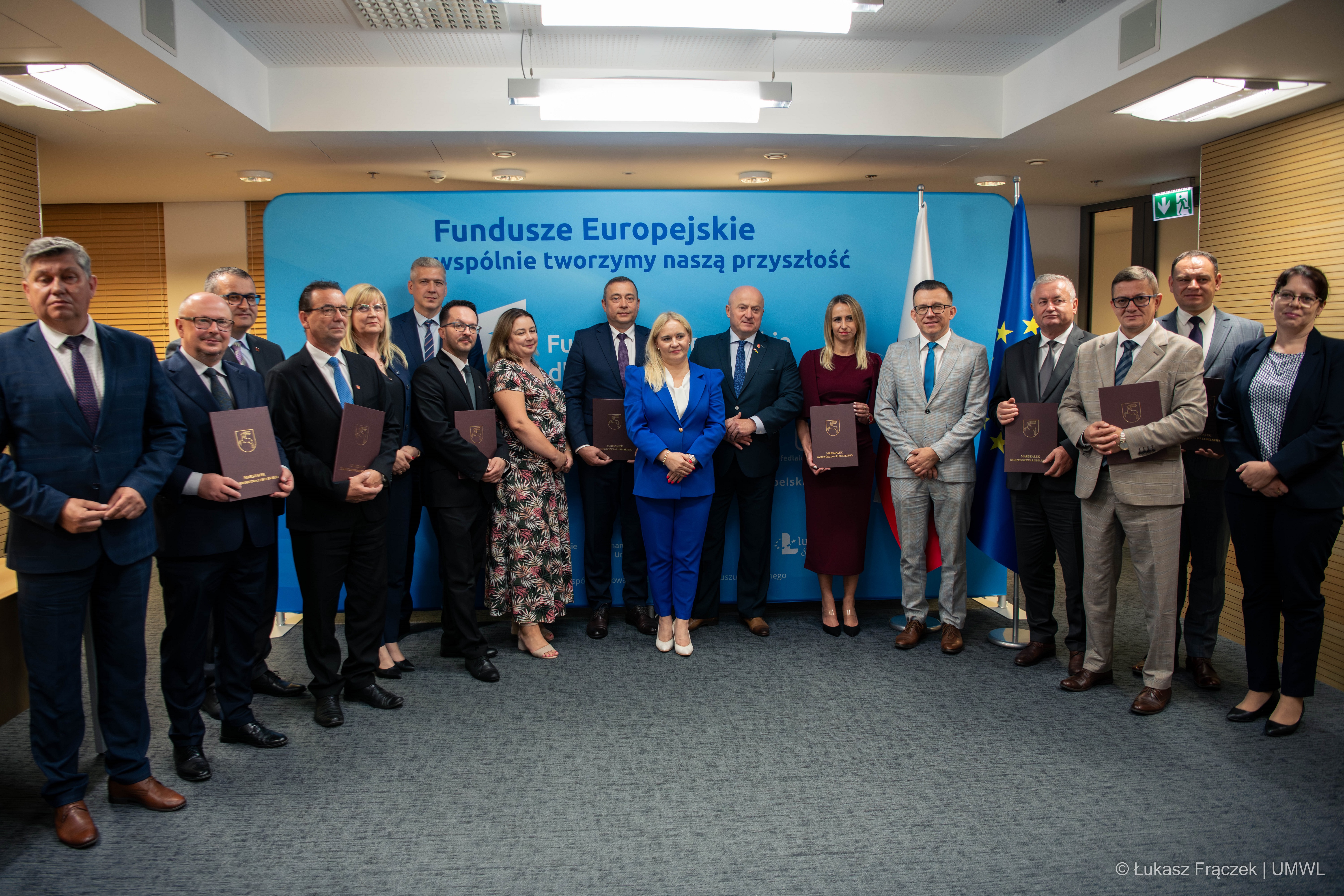 Wszyscy beneficjenci pozują wspólnie do zdjęcia z marszałkiem WL. Łącznie na zdjęciu znajduje się kilkanaście osób stojących w półkole w sali konferencyjnej