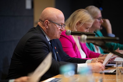 Na pierwszym planie marszałek Jarosław Stawiarski siedzi przy biurku i udziela wypowiedzi do mikrofonu. W tle widać kilka siedzących osób