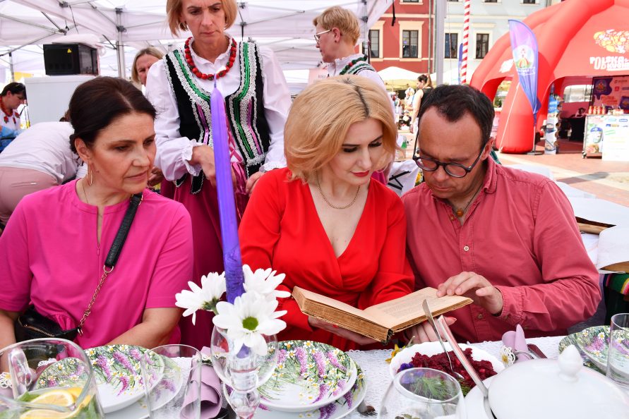 Zdjęcie przedstawia trzy osoby, dwie przeglądają trzymaną w ręku starą książkę.