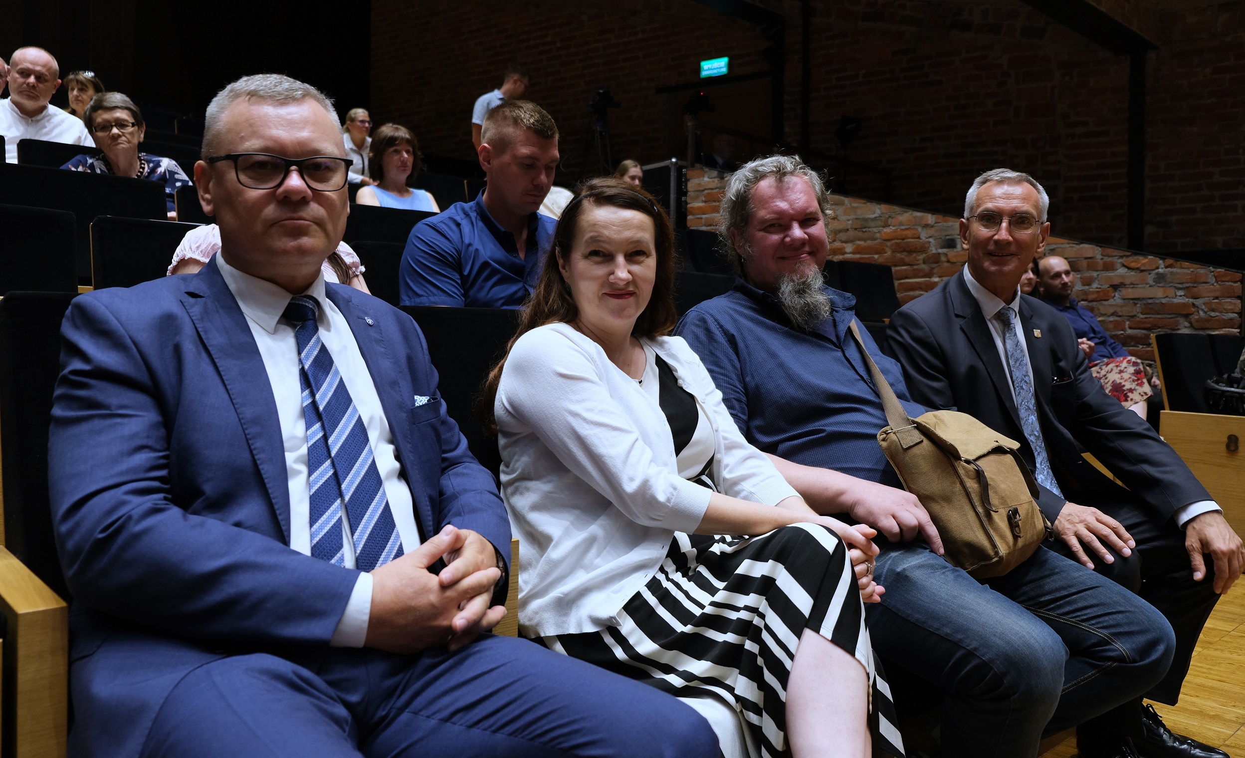 Widok na cztery osoby siedzące na widowni jedną kobietę i trzech mężczyzn