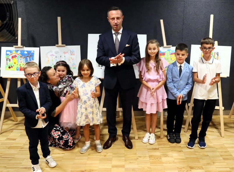 Pamiątkowe zdjęcie dzieci z wicemarszałkiem Mulawą na tle sztalug z nagrodzonymi pracami