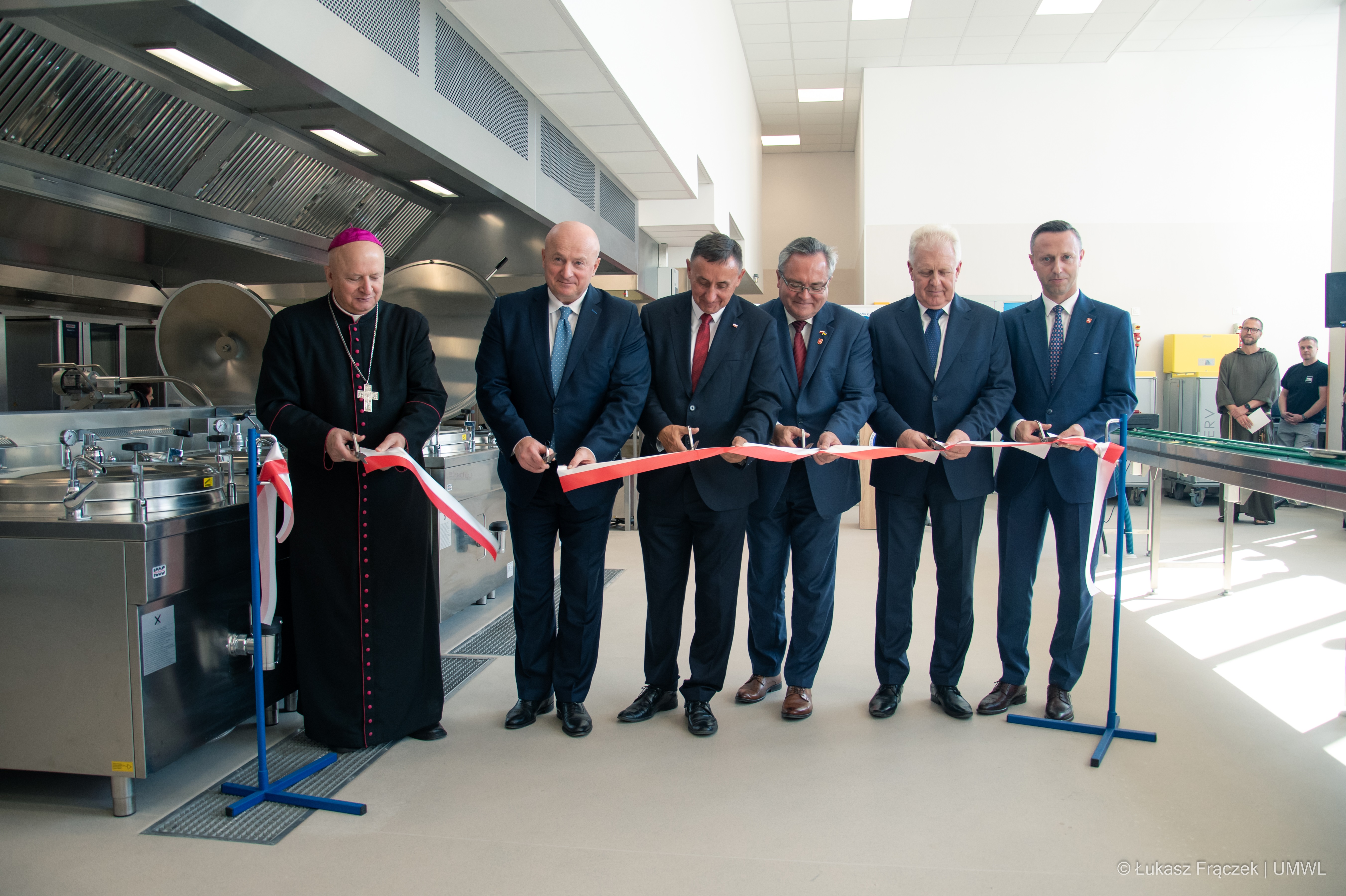 Przedstawiciele władz samorzadowych, zarzadu szpitala i władz duchownych - sześciu mężczyzn przecina wstęgę podczas otwarcia pralni i kuchni w szpitalu