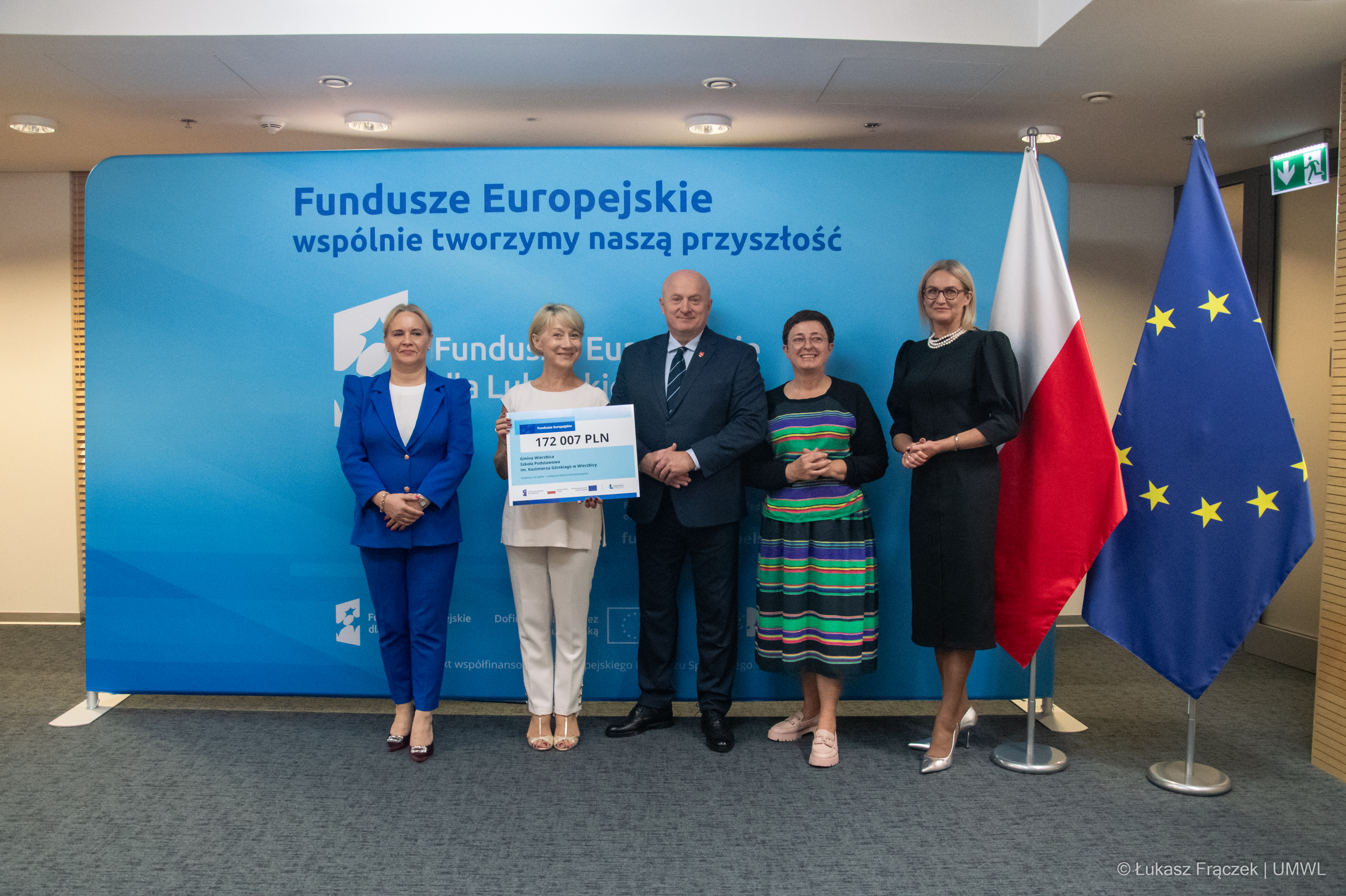 Grupa osób pozuje do zdjęcia w sali konferencyjnej , za nimi stoi ścianka z Funduszami Europejskimi