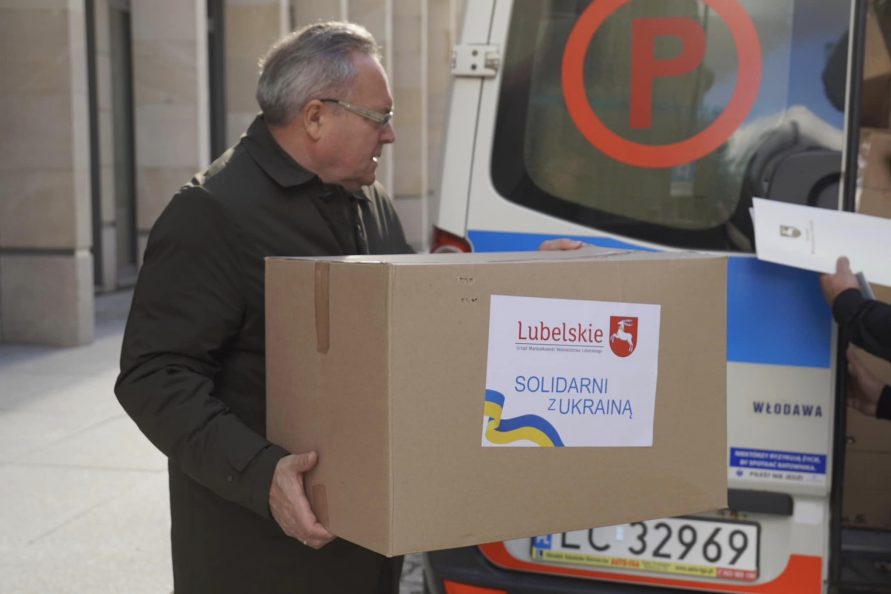 Zbigniew Wojciechowski wicemarszałek niesie pudło tekturowe z napisem Solidarni z Ukrainą