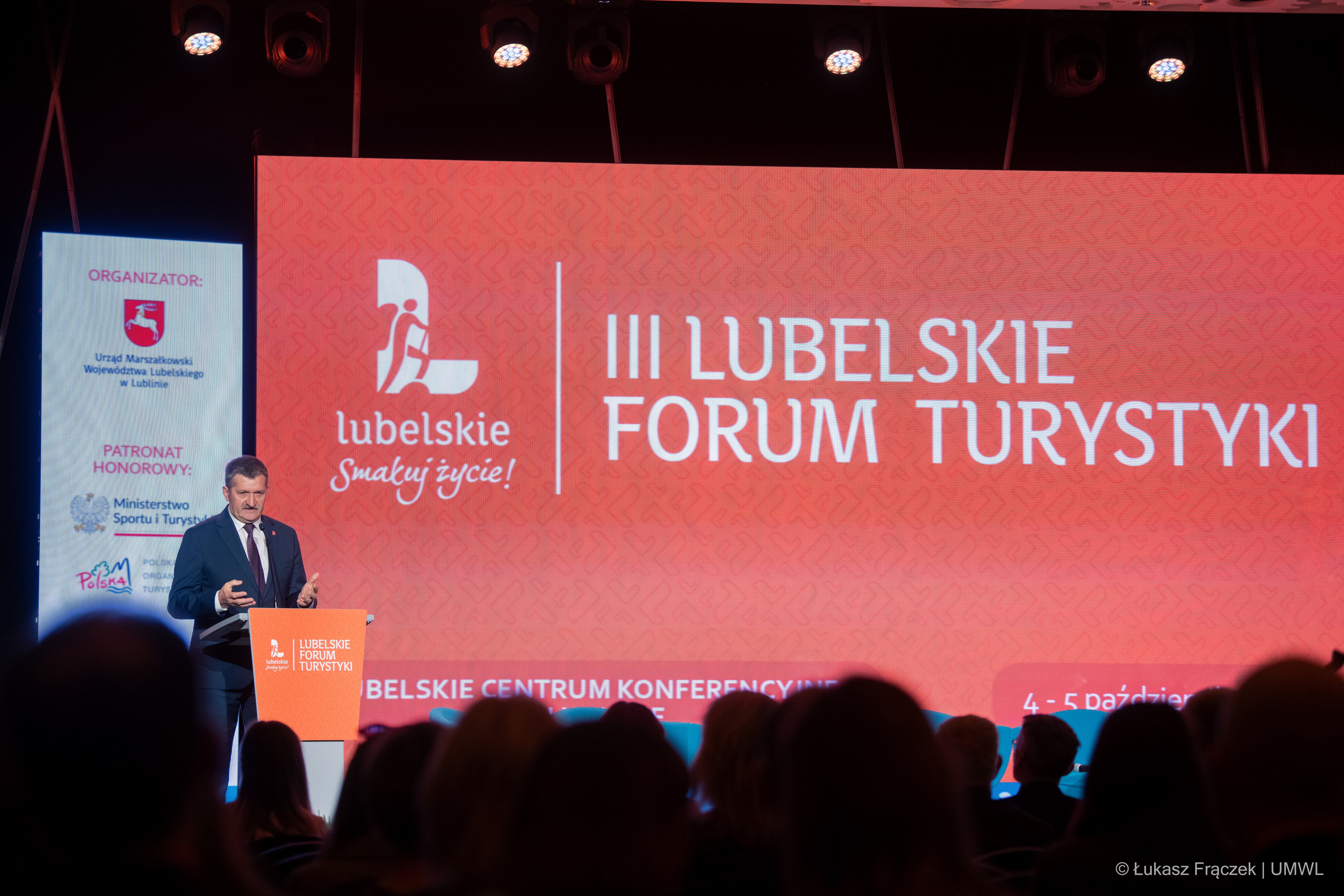 Członek Zarządu Zdzisław Szwed stoi przy mównicy i otwiera wydarzenie, za nim na ekranie wyświetla się napis III Lubelskie Forum Turystyki