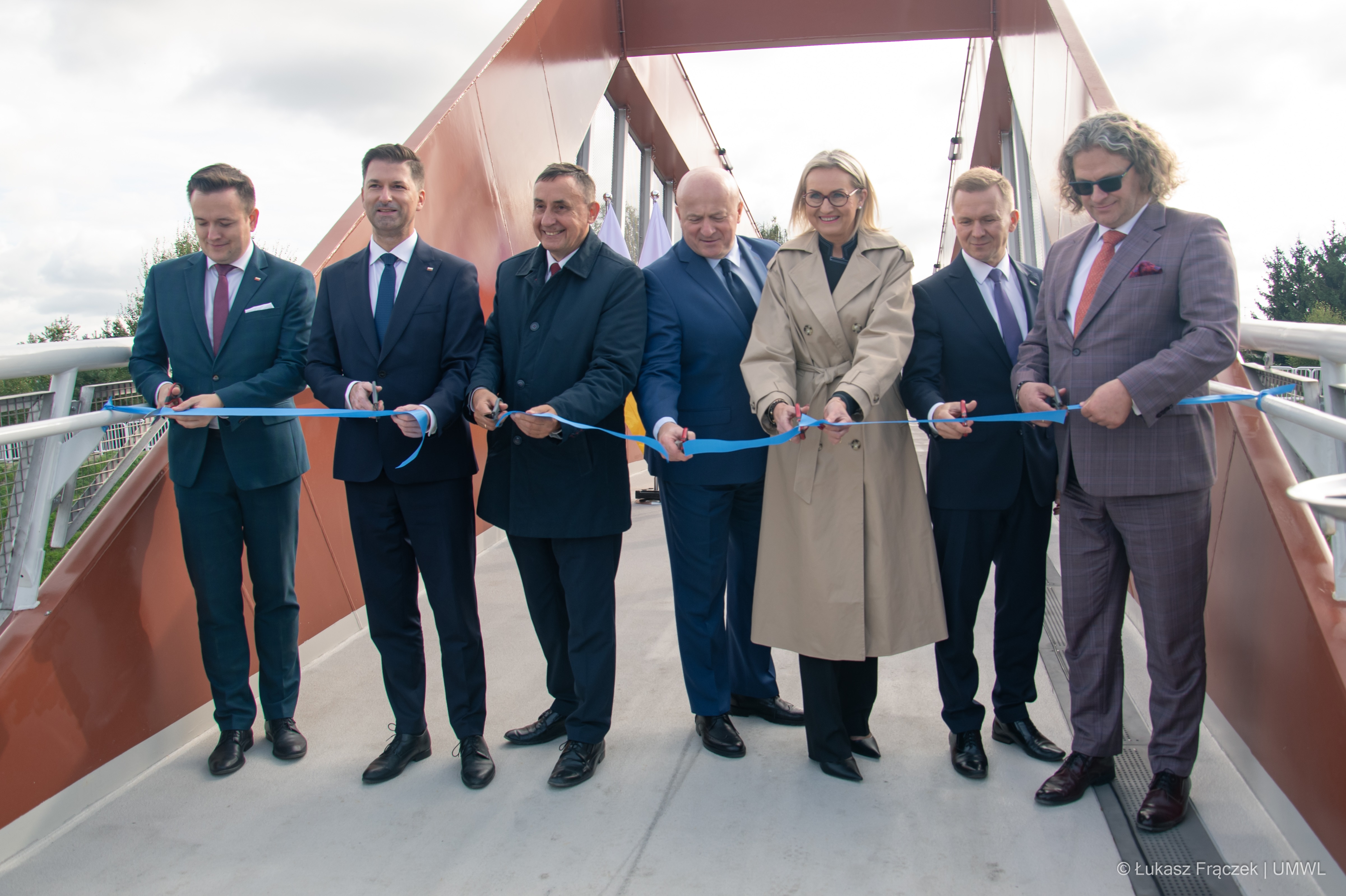 Sześciu mężczyzn i jedna kobieta, przedstawiciele władz samorządowych iprzecinają wstęgę na otwarciu kładki