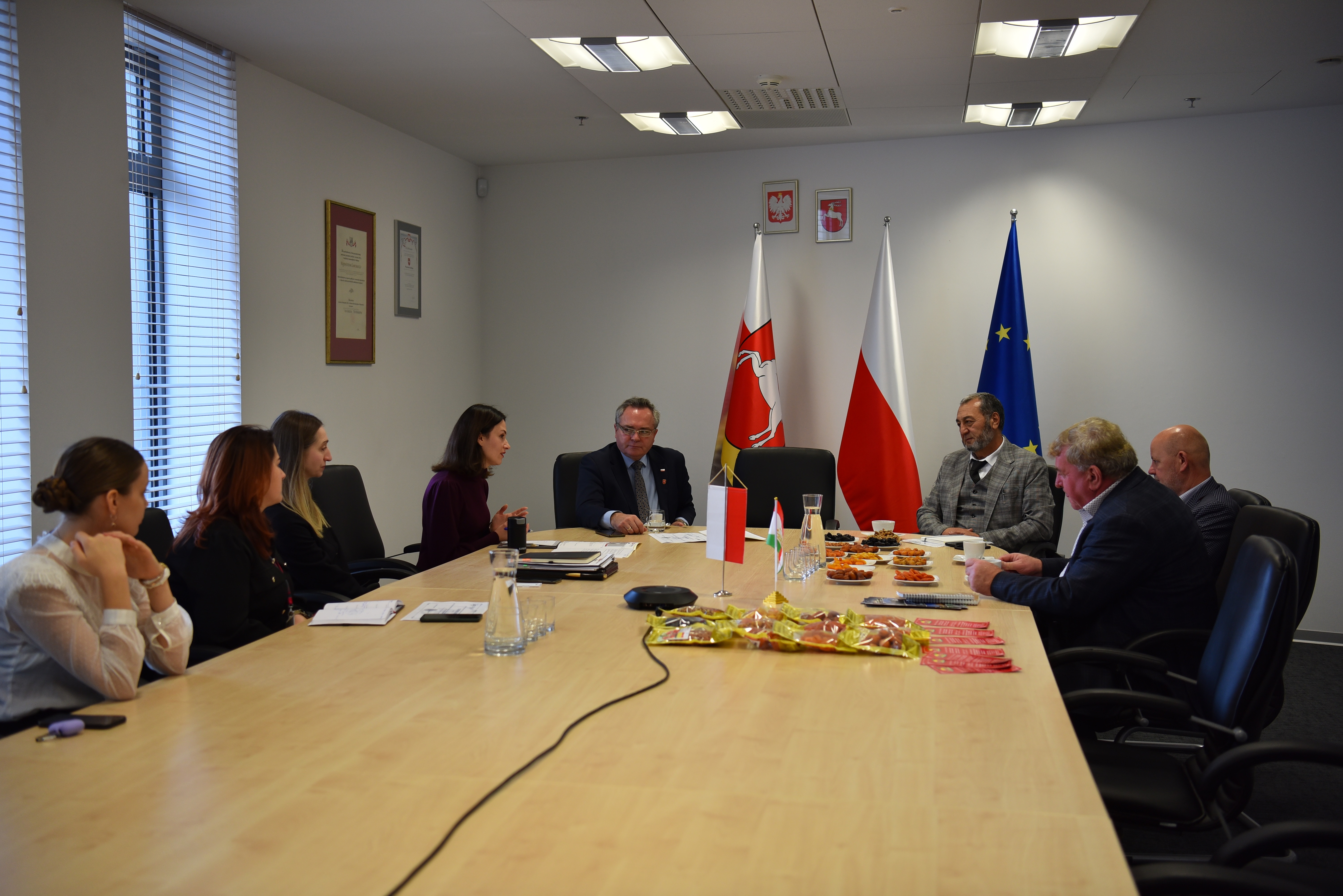 widok na salę konferencyjna i kilka osób siedzących przy stole, na którym są rozłożone talerze z suszonymi owocami