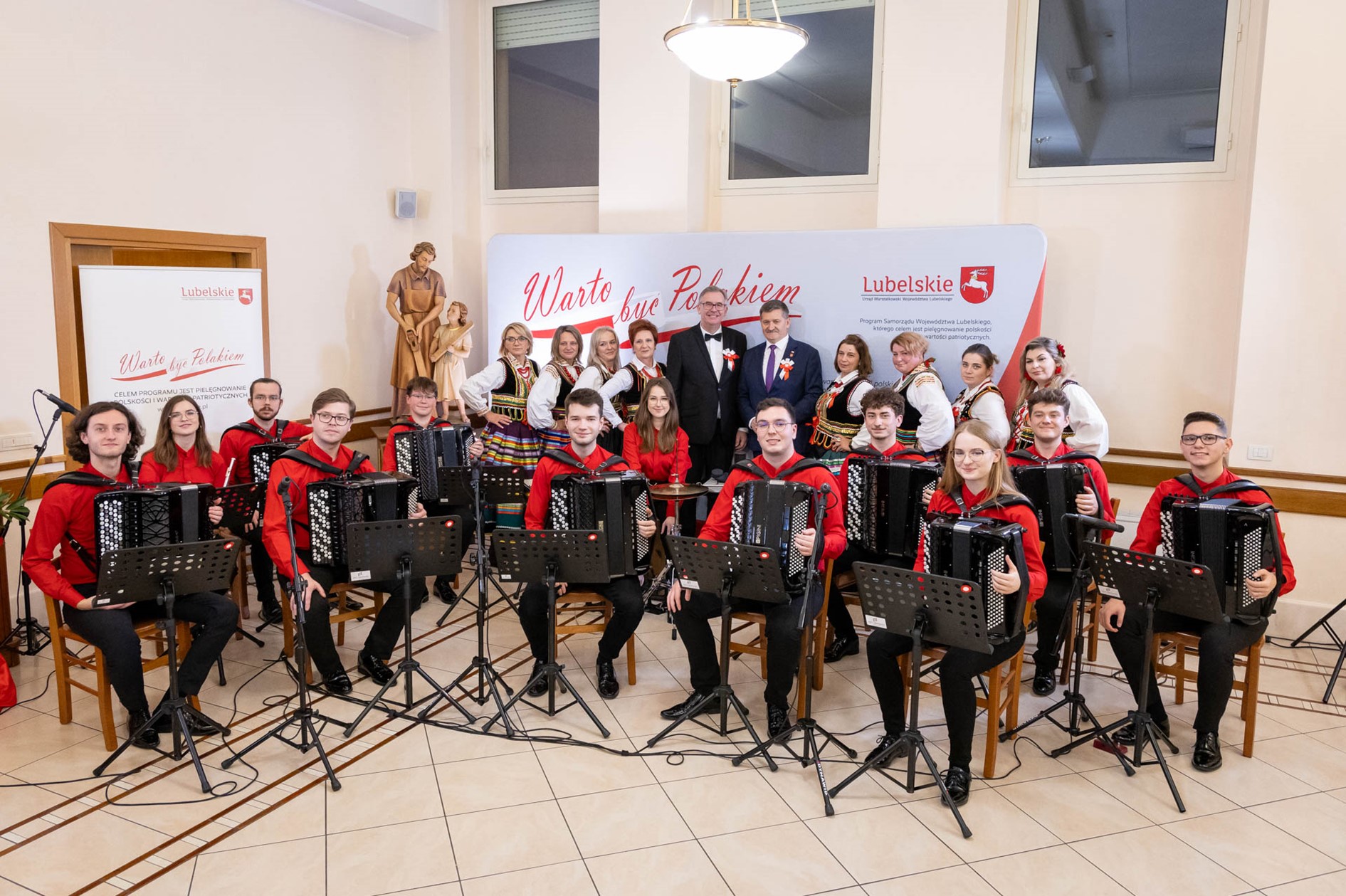 Grupa osób które siedzą krzesłach trzymając instrumenty muzyczne.