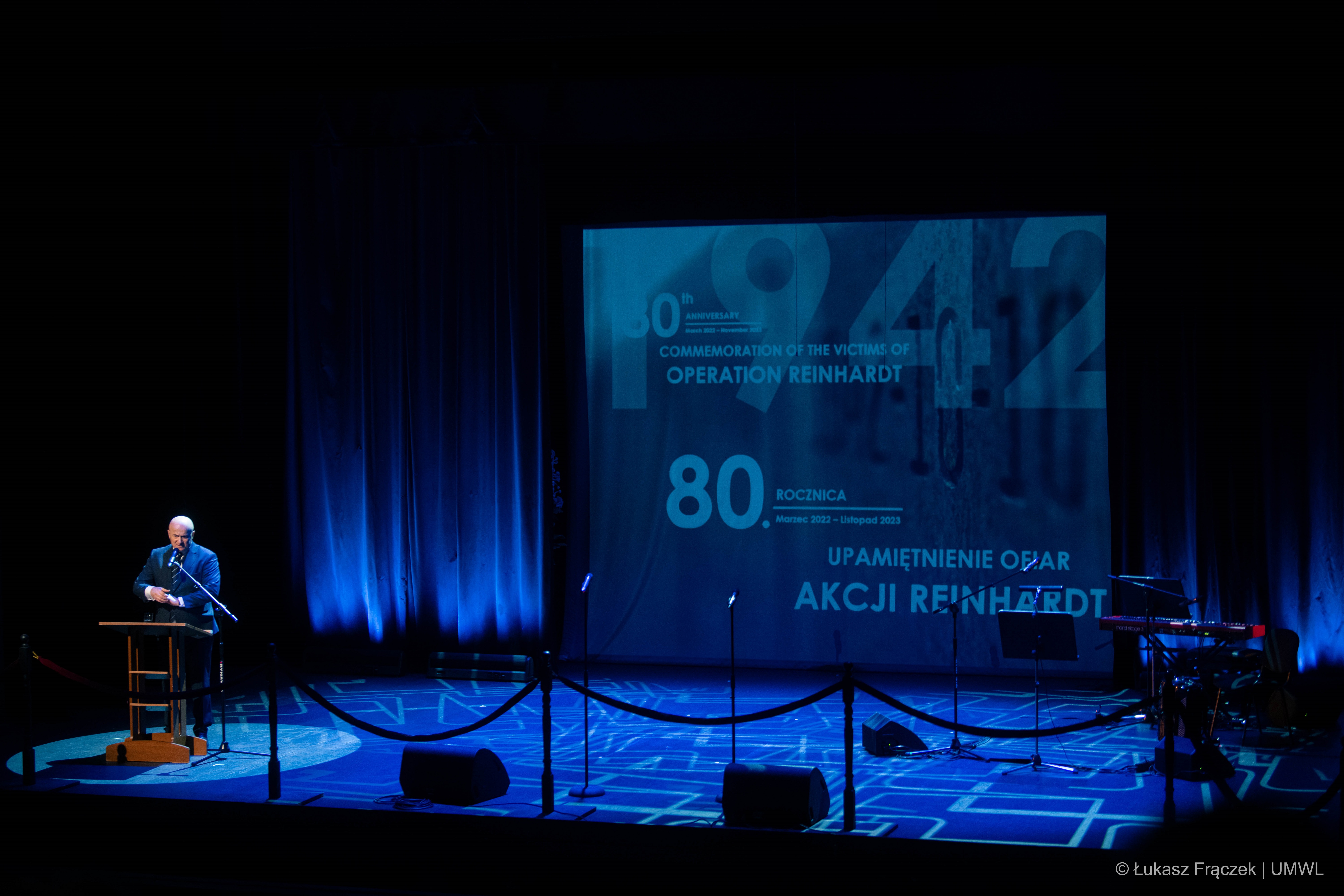 widok na scenę z ekranem wyświetlającym informację o 80. rocznicy akcji Erntfest w rogu sceny stoi Marszałek województwa lubelskiego i udziela wypowiedzi w kierunku widowni