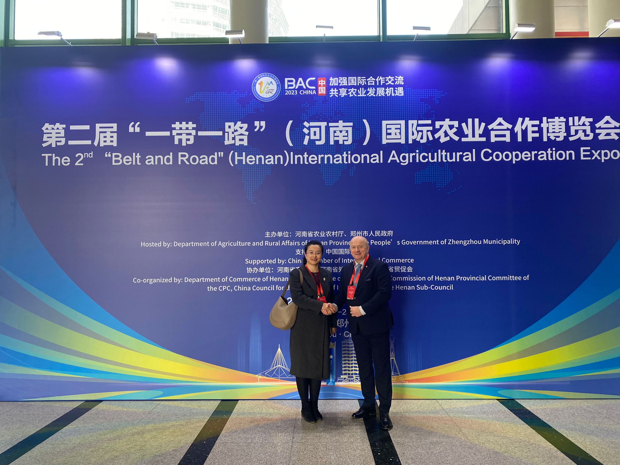 Marszałek Jarosław Stawiarski stoi na ściance z napisami w języku chińskim, towarzyszy mu kobieta