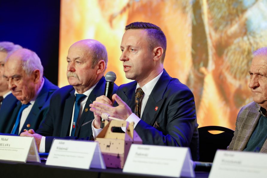 Wicemarszałek Michał Mulawa podczas konferencji siedzi w towarzystwie kilku innych mężczyzn i udziela wypowiedzi do mikrofonu