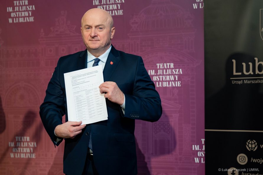 Marszałek Jarosław Stawiarski stoi na ściance Teatru Osterwy i pokazuje trzymany w rękach dokument