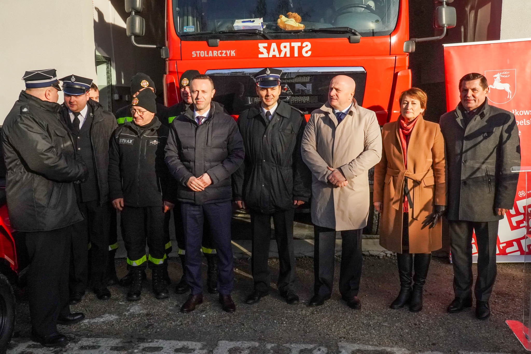Około sześciu osób stojących na dworze przed wozem strażackim. Wśród nich stoi marszałek Jarosław Stawiarski