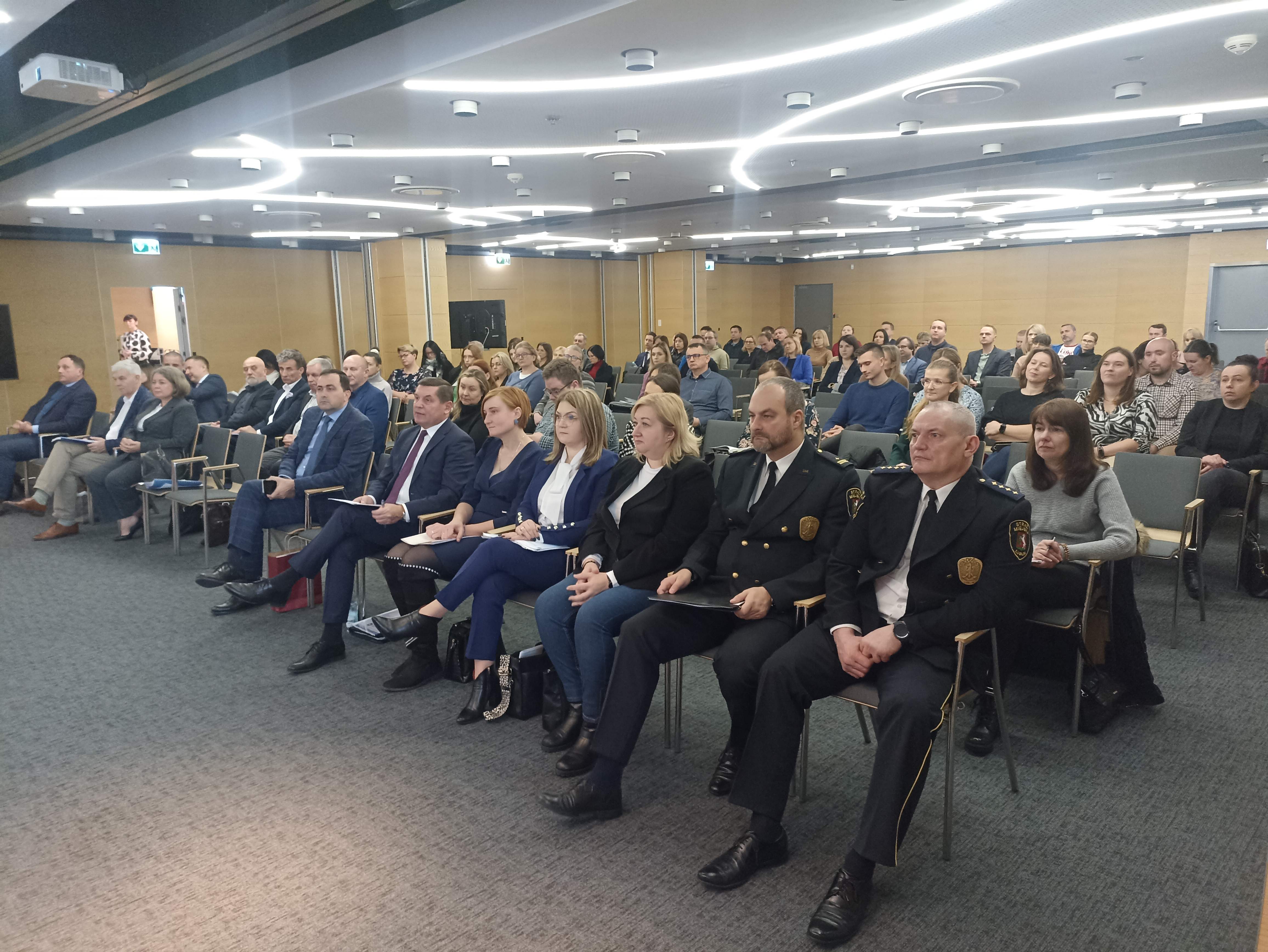 Widok na publiczność w sali konferencyjnej. Kilkadziesiąt osób siedzi w kilku rzędach.