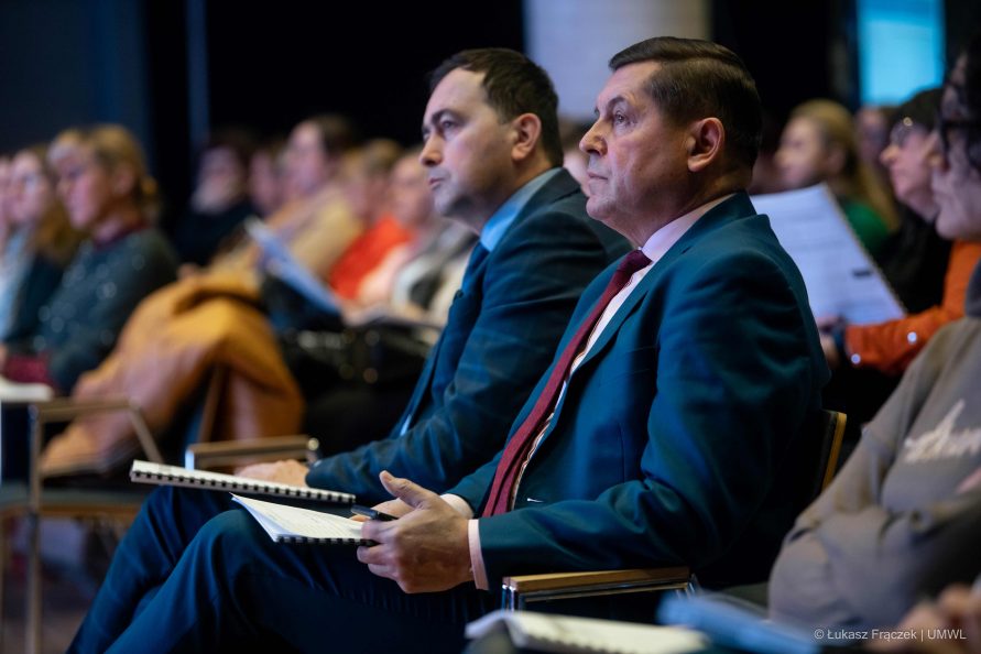 Widok na salę konferencyjną. Na pierwszym planie dwóch słuchaczy konferencji