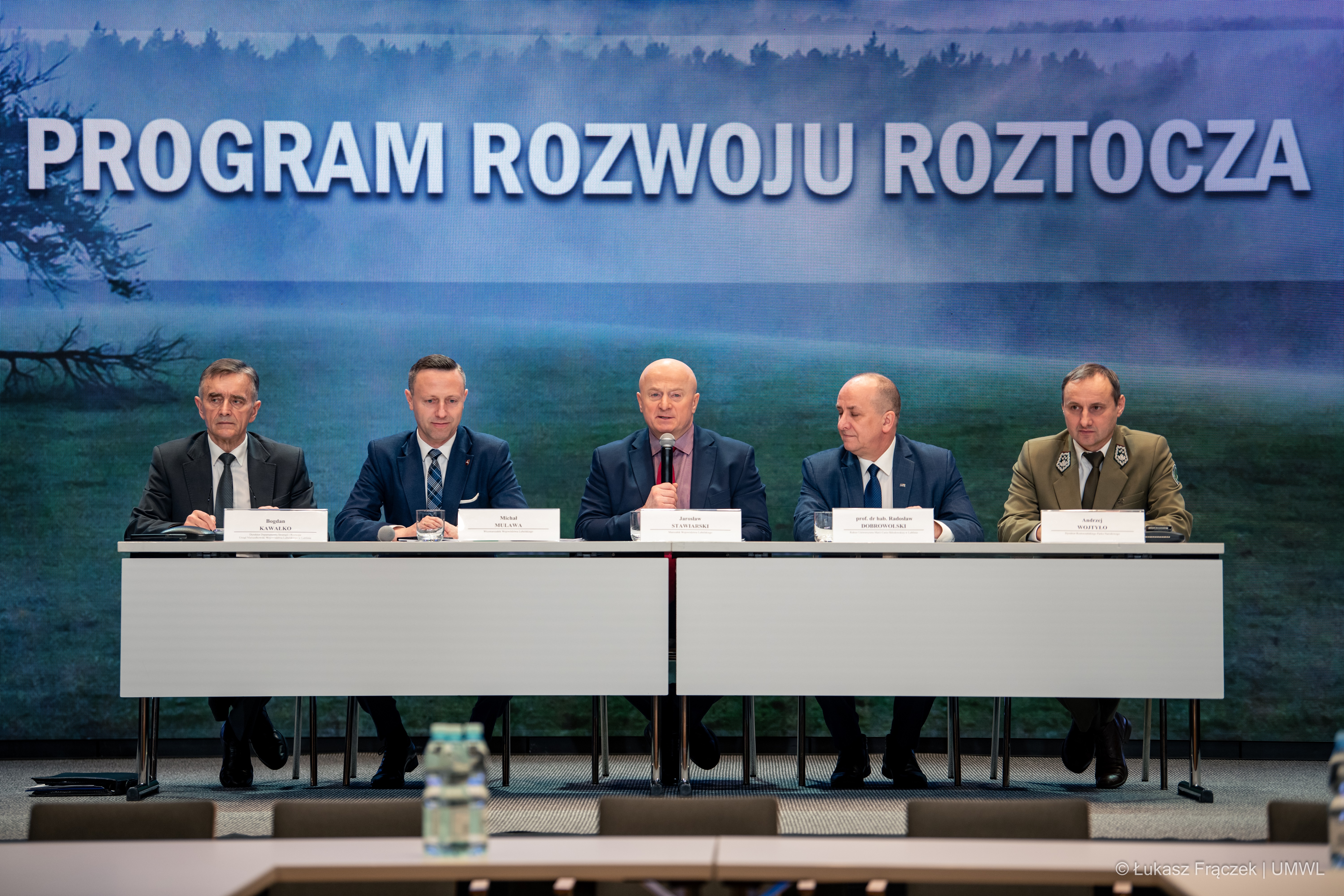 uczestnicy konferencji siedzą przy stolikach za nimi znajduje się ekranz grafiką i napisem Program rozwoju Roztocza