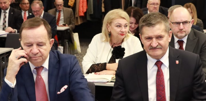 Na zdjęciu widoczni są dwaj elegancko ubrani mężczyźni (garnitury, białe koszule, krawaty), którzy prawdopodobnie siedzą przy stole. Jednym z nich jest Zdzisław Szwed, Członek Zarządu Województwa Lubelskiego. W tle kobiety i mężczyźni także siedzący przy stolikach.