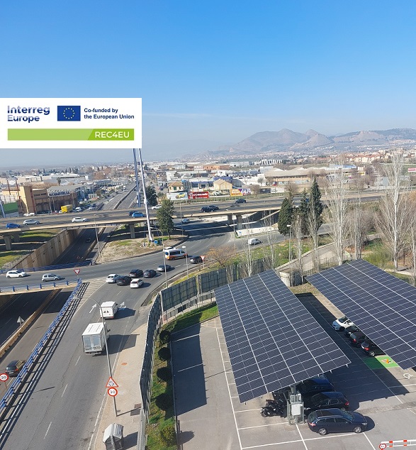 Widok z dachu na parking z panelami fotowoltaicznymi. W prawym górnym rogu logo projektu, nazwa projektu z zielony pasek symbolizujący priorytet srodowisko.